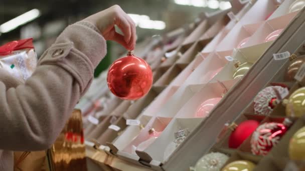 Bayan müşteri Noel ağacında Noel oyuncaklarını seçiyor evi dekore etmek ve perakende mağazasında şenlikli bir ortam yaratmak için, yakın çekim için. — Stok video