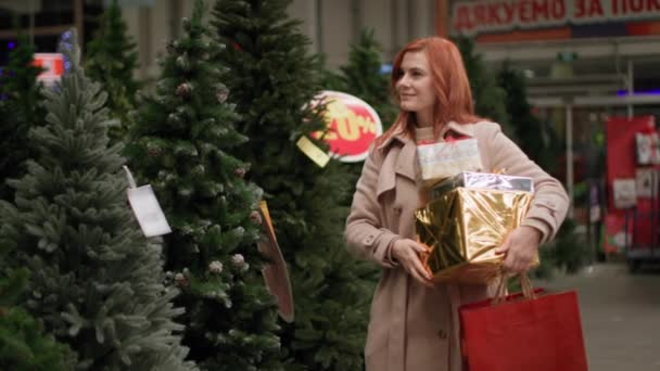 Újévi ünnepek, egy bájos női ügyfél úgy dönt, egy mesterséges karácsonyfa egy áruházban, hogy hozzon létre egy ünnepi hangulatot otthon, és mentse a természetet, szöveg jelenik meg klip mondat: köszönöm — Stock videók