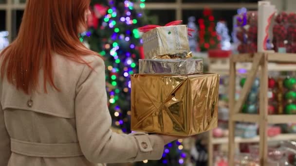 Zakupy noworoczne, radosna kobieta z zakupami w rękach uśmiecha się i patrzy w kamerę na tle choinki w sklepie — Wideo stockowe