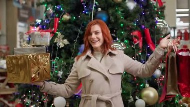 Satışlar, elinde alışverişlerle mutlu bir kadın mağazadaki satın alınan mallara bayılıyor, gülümsüyor ve kameraya başparmak işareti yapıyor.