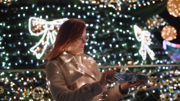 Sărbători fericite de iarnă, o femeie frumoasă deschide visător fundalul cadou al unui brad de Crăciun al orașului decorat cu ghirlande în noaptea de Crăciun — Videoclip de stoc