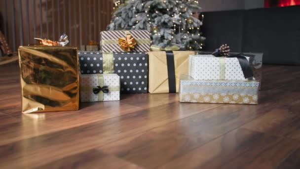 Remaja laki-laki lucu yang menggemaskan bersembunyi mengintip dari bawah dibungkus hadiah berbaring di lantai di depan pohon Natal, tersenyum dan melihat kamera — Stok Video