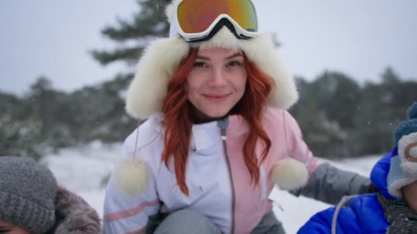 Felices vacaciones de invierno en el bosque al aire libre, primer plano mamá mira a la cámara y luego ayuda a sus hijos en un trineo por el tobogán — Vídeos de Stock