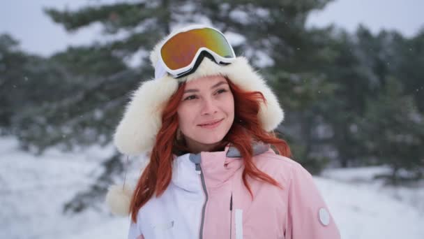 Χειμερινό πορτρέτο του ευτυχισμένου κοριτσιού με μάσκα του σκι και καπέλο κοιτάζει την κάμερα στο φόντο του χιονιού στο δάσος — Αρχείο Βίντεο