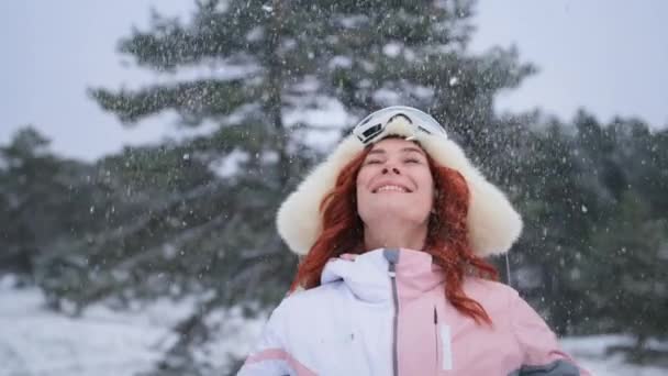 Chica lanza nieve en el aire, retrato de invierno de mujer joven feliz en un pasamontañas y un sombrero mira a la cámara y sonríe en el bosque — Vídeos de Stock