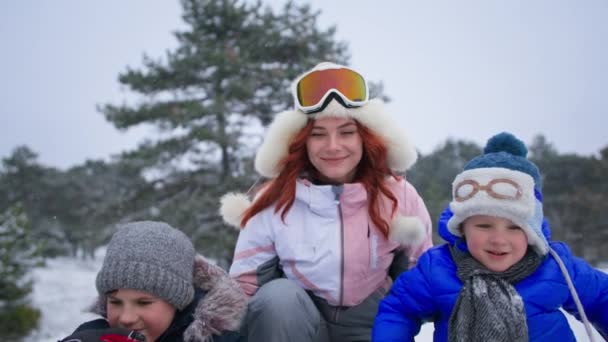 Διασκεδαστική διασκέδαση για τη μητέρα και τα παιδιά, ευτυχισμένη νεαρή γυναίκα βοηθά τους γιους της πάει κάτω από το λόφο με έλκηθρο το χειμώνα, κορίτσι παλαμάκια χέρια — Αρχείο Βίντεο