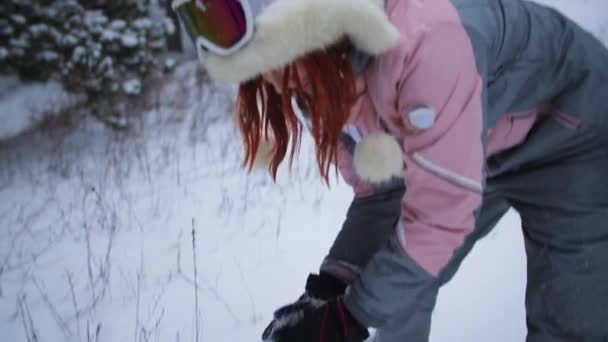 Menina feliz em um chapéu quente e luvas faz uma bola de neve e joga perto da câmera, fim de semana ativo na floresta — Vídeo de Stock