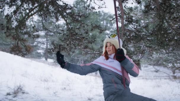 森の中のスイングに携帯電話に乗って暖かい帽子の現代の女の子,若い女性は冬の性質を楽しんで、ソーシャルネットワークのためのビデオ録画を行います — ストック動画