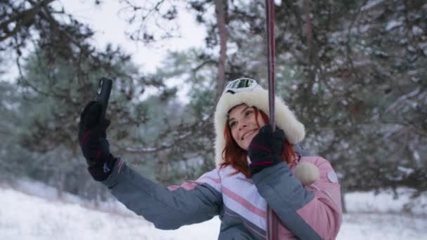 Menina com smartphone em suas mãos grava um vídeo enquanto monta um balanço na floresta, uma jovem mulher com um gadget está descansando ao ar livre no inverno — Vídeo de Stock