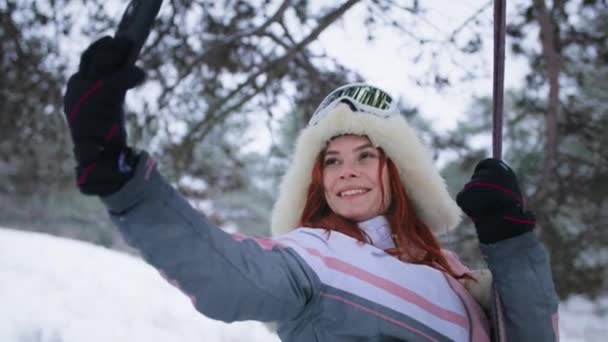 Dziewczyna w zimie nagrywa wideo na telefon komórkowy podczas jazdy na huśtawce w lesie, młoda kobieta w ciepłych ubraniach z gadżetem spoczywa na zewnątrz — Wideo stockowe