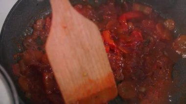 Ev yemeği, sebzeli domates sosu sıcak makarna tavasında ahşap bir spatulayla karıştırılır.