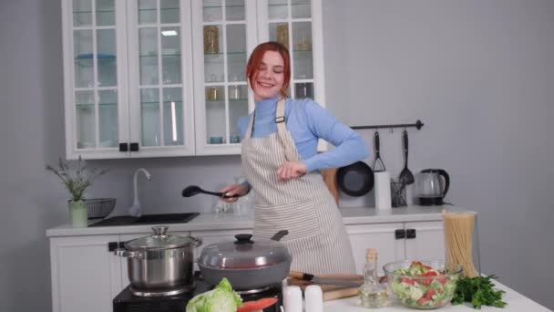 Jong huisvrouw het hebben van plezier dansen en zingen tijdens het bereiden van voedsel voor haar familie in de keuken thuis — Stockvideo