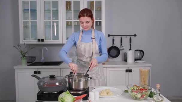 Hemlagad mat, en ung hemmafru tar pasta ur pannan och lägger den på familjens serveringstallrik stående i köket. — Stockvideo