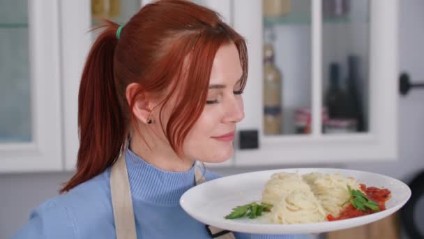 Italian food, portrait of beautiful female cook with a plate of spaghetti with sauce in her hands stands background of kitchen, smiles and looks at camera — Stock Video