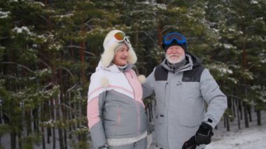 Sıcak kıyafetler ve kayak gözlüğü takan yaşlı bir çiftin portresi. Ormanın arka planında birbirlerine sarılıyorlar. Emekliler kışın dışarıda vakit geçiriyorlar.