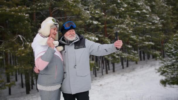 幸せな結婚、古い配偶者は森の中で新鮮な霜の空気を楽しみ、携帯電話で写真を撮る、妻は彼女の夫にキス — ストック動画