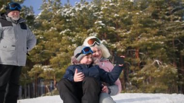 Torunu olan aktif bir büyükanne kızakla tepeden kayıyor, cep telefonlu bir çocuk karlı bir ormanda büyük anne ve babasıyla eğlenirken video çekiyor.