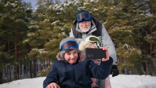 Boy child with mobile phone shoots a video when sleds down a hill with an elderly grandmother, grandparents have fun with their grandson in the forest — Stock Video