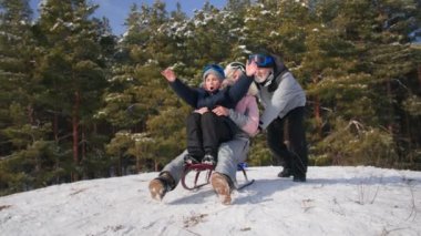 Büyükanne ve büyükbaba, kışın karlı bir ormanda torunlarıyla birlikte eğleniyorlar. Büyükannesi olan bir çocuk ellerini kaldırıp kızakla tepeden aşağı kayıyor.