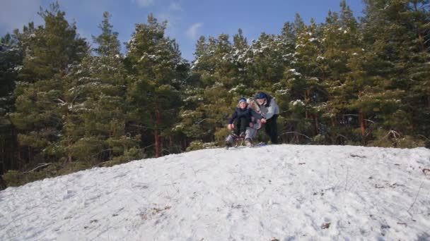 Eldre mann hjelper sønnesønn med å gå ned bakke på slede med bestemor i skogen, god vinterhelg med familien – stockvideo