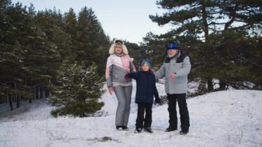 Büyük anne ve büyük baba ve torun, kış ormanlarının güzelliklerine bakıyorlar. Küçük çocuk, karlı bir tepede dururken büyükbabasıyla büyükannesine sarılıyor.