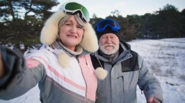 Emekliler karlı bir ormanda cep telefonuyla iletişim kuruyor. Sıcak kıyafetler ve kayak gözlüğü takmış yaşlı bir çift kameraya ellerini sallayıp sarılıyorlar.