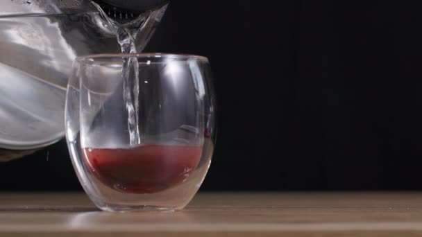 Delicioso chá de vitamina de frutas saudáveis em um copo transparente é derramado com água quente em um fundo escuro — Vídeo de Stock