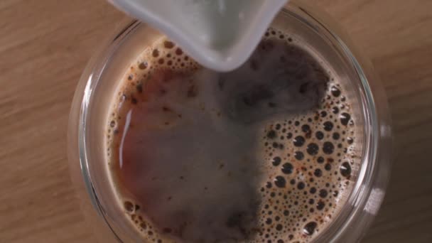 Vista dall'alto, delizioso latte schiumato da una brocca di latte viene versato nel caffè per ottenere un latte o un cappuccino a casa, primo piano — Video Stock