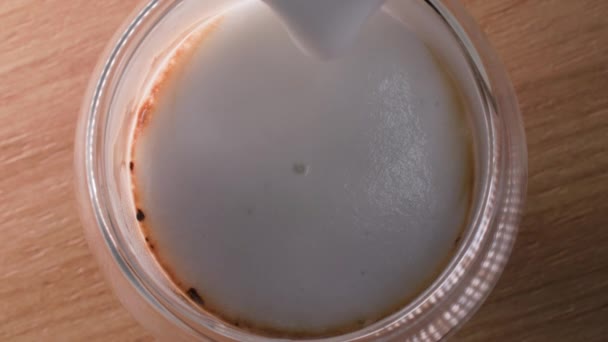 Läcker aromatisk dryck, skummad mjölk från en mjölkkanna hälls i kaffe i ett genomskinligt glas, ovanifrån — Stockvideo
