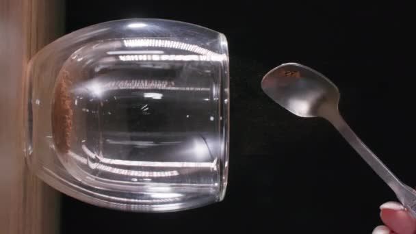 Bereiding van een drankje, instant koffie wordt gegoten in een transparant glas en gegoten met warm water, close-up, verticaal scherm — Stockvideo
