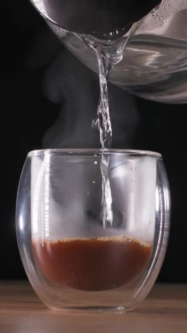 Hot steaming water is poured into instant grains to obtain a coffee drink in a transparent glass, vertical screen — Stock Video
