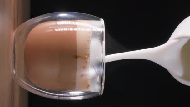 Cappuccino 's, heerlijke aromatische koffiedrank giet melkschuim uit een melkkan in een transparant glas, verticaal — Stockvideo