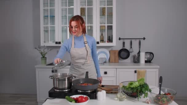 Joven mujer preparando la cena para su familia lanza sal en una cacerola y arroja verduras de colores en un exprimidor mientras está de pie en la cocina — Vídeos de Stock