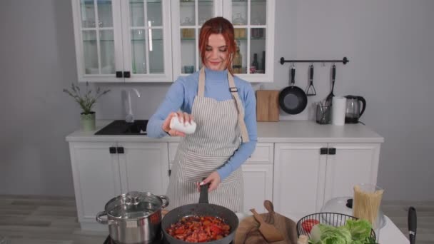 Végétarisme, une cuisinière dans un tablier prépare des légumes colorés dans une poêle jette des épices tout en restant debout dans la cuisine — Video