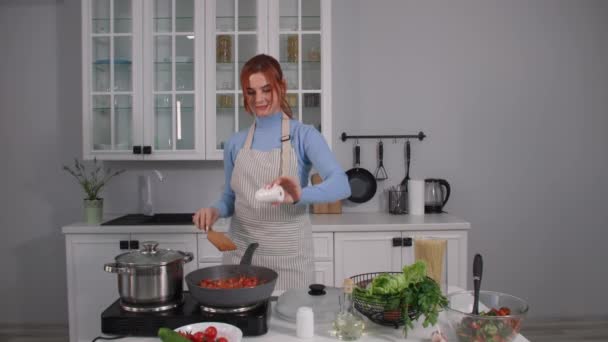 Cocina vegetariana, mujer joven en un delantal cocina verduras de color guisado en una sartén caliente en una estufa eléctrica mientras está de pie en la cocina en casa — Vídeos de Stock