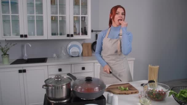 Wesoła kobieta kroi świeże warzywa do sałatki podczas gotowania wrzuca do miski, uśmiecha się i patrzy w kamerę — Wideo stockowe