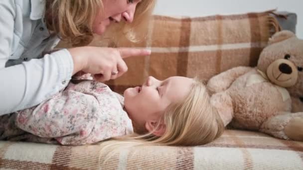 Macierzyństwo, kochająca mama bawi się z ukochaną córką i delikatnie dotyka nosa w nos podczas zabawy na kanapie w domu — Wideo stockowe