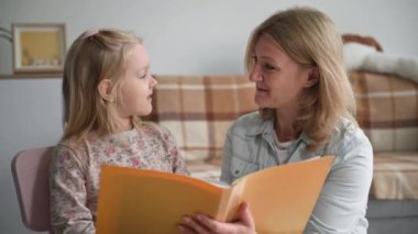 Çocuk gelişimi, elinde kitap olan ilgili bir kadın küçük bir kıza rahat bir odada ders sırasında okumayı öğretiyor.