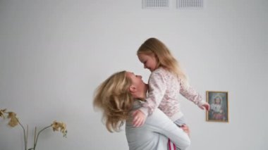 Neşeli küçük kız, annesinin kollarında mutlu bir anın tadını çıkarıyor. Sevecen bir kadın, evde dinlenirken sevimli bir kızın kollarında dönüyor.