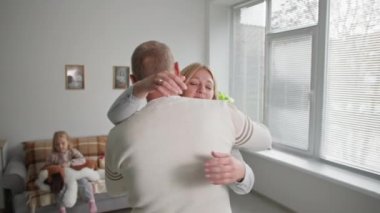 Aile refahı, neşeli eş sevgili kocasıyla tanışıyor ve ona sarılıyor. Odadaki kanepede oturan kadın çocuğunun arka planı.