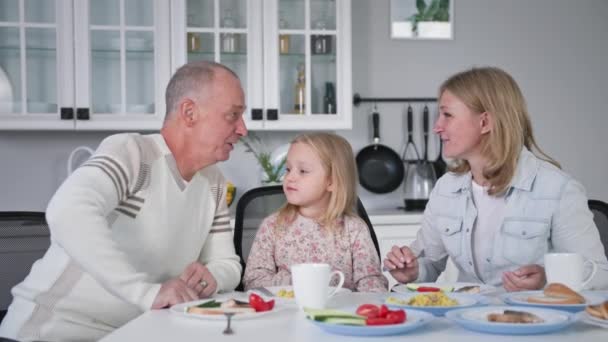 Egyesült család, szerető szülők és imádnivaló lányuk jól érzik magukat az ebédnél a konyhában ülve. — Stock videók