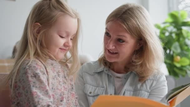 Moederschap, liefdevolle moeder leest boek met haar mooie dochter en verheugt zich en lacht als vrouwelijke kind niest, close-up — Stockvideo