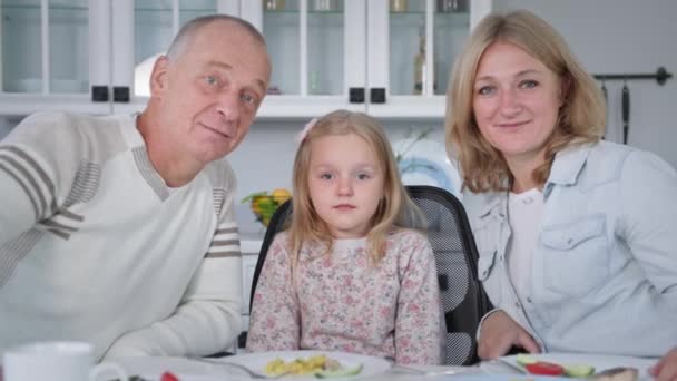 Fröhliche Familie, glückliche Eltern mit ihrer Tochter unterhalten sich am Tisch beim Abendessen in einer gemütlichen Küche — Stockvideo