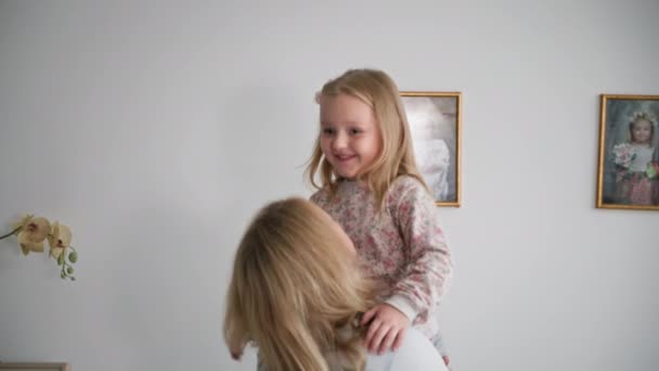 Счастливая маленькая девочка веселится с протянутыми руками, сидя в объятиях любящей матери, расслабляясь дома — стоковое видео