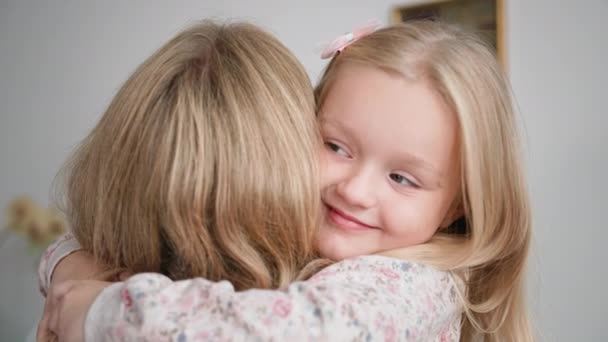 Щаслива сім'я, чарівна усміхнена маленька дівчинка з любов'ю і ніжністю обіймає свою люблячу матір, відпочиваючи вдома — стокове відео