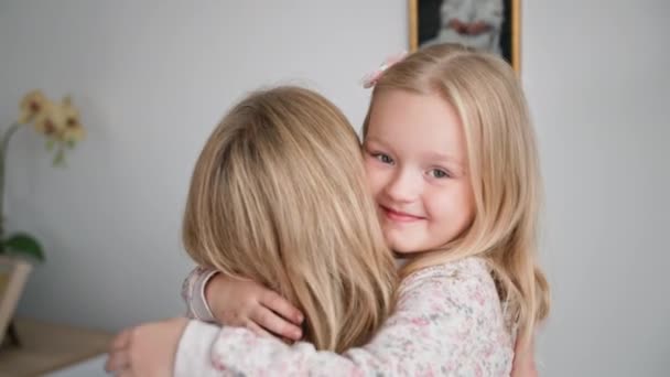 Дочь матерей, любящая маленькая девочка с любовью обнимает женщину-родителя наслаждаясь моментом, улыбается и смотрит в камеру — стоковое видео