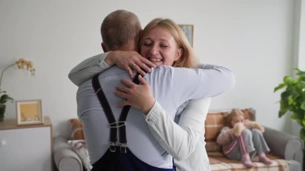 幸福的家庭，充满爱心的快乐的妻子抱着女儿的背景在舒适的房间沙发上迎接她的丈夫 — 图库视频影像