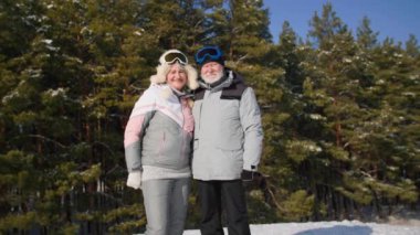 Güneşli bir havada kış ormanında yürürken gülümseyen ve kameraya bakan sevimli emeklilerin portresi.