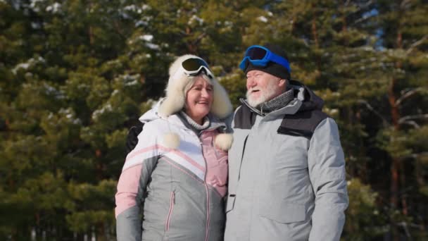 雪の中の晴れた日に老人と最愛の妻が森の中で一緒に休んでカメラを見て笑っています — ストック動画