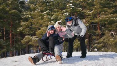 Açık hava aktiviteleri, yaşlı bir kadın ve bir erkek ve bir torun bir kızağa biniyor ve kar ve ağaçların arasında kış ormanlarında dinlenirken akıllı telefon kullanarak iletişim kuruyor.